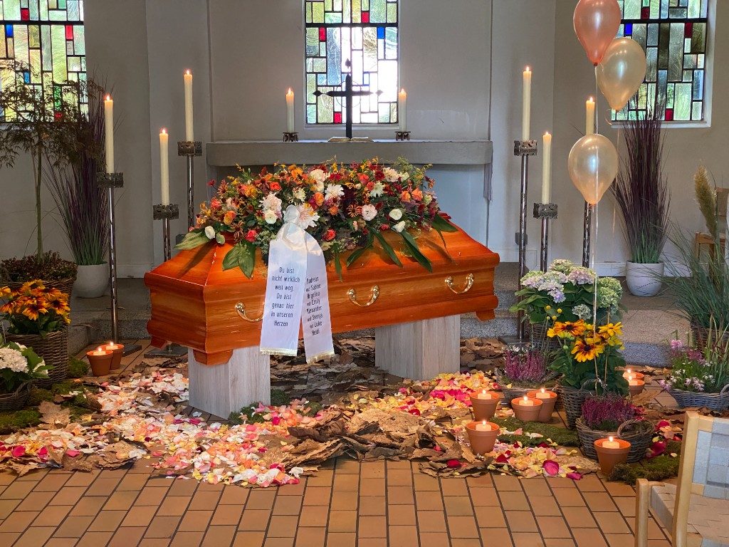 Sarg mit herbstlichem Blumenschmuck, Luftballons und Rosenblättern in der Kapelle